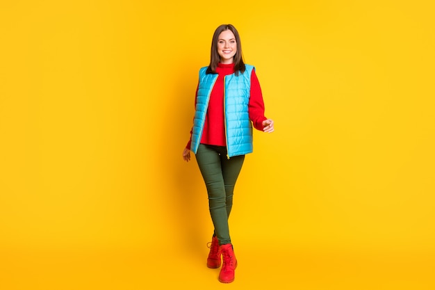 Photo de toute la taille du corps d'une jolie jeune femme souriante souriante marchant élégamment sur la pointe des pieds vers vous portez un pantalon vert gilet bleu pull rouge bottes isolées fond de couleur jaune vif