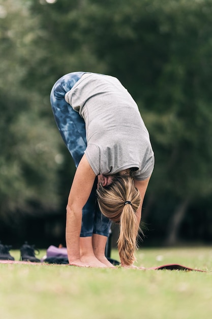Photo verticale d'une femme blonde faisant des étirements dans une position de yoga dans un parc