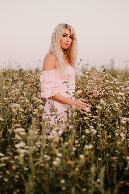 Photo verticale femme blonde posant dans le grand champ sans fin de marguerites en soirée d'été