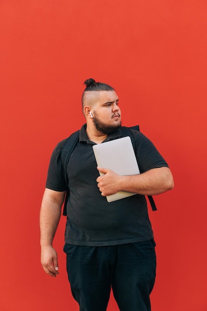 Photo verticale d'un gros étudiant avec une barbe debout sur un fond de mur rouge