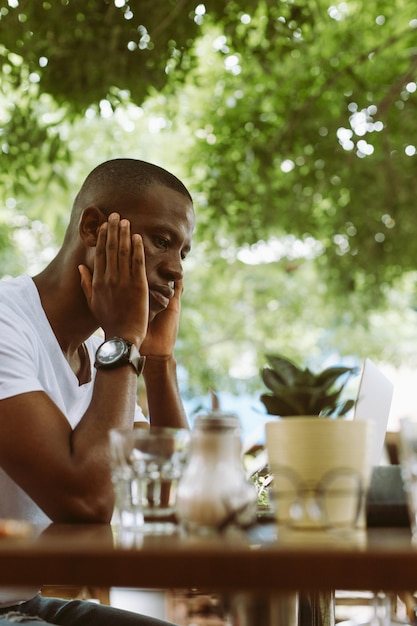 Photo photo verticale d'un homme multiracial confus avec un ordinateur portable dans un café ne sais pas quoi faire avec la tête dans le han