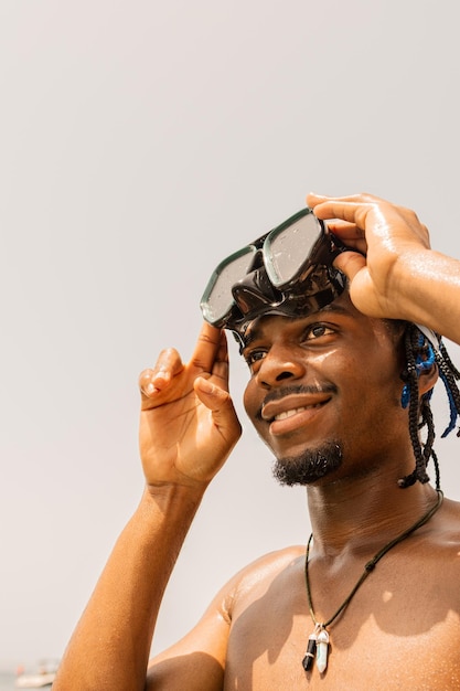 Photo verticale d'un homme noir heureux sur la plage avec ses lunettes de plongée sur la tête