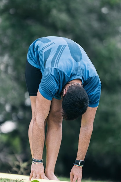 Photo verticale d'un homme sportif faisant des étirements dans une position de yoga dans un parc