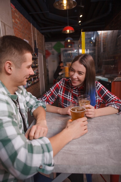 Photo verticale d'un jeune couple appréciant de boire de la bière ensemble à une date au pub