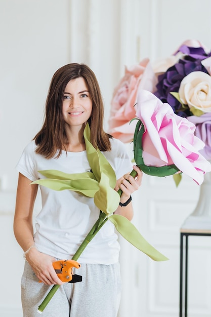 Photo verticale d'une jeune designer ou fleuriste professionnelle tenant un grand bouquet utilise des pinces de jardin vêtues d'une tenue décontractée aime la décoration possède un magasin de fleurs d'affaires fait des arrangements