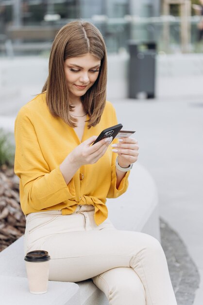 Photo verticale d'une jeune femme caucasienne blanche tenant une carte de crédit à l'aide d'un appareil mobile numérique et b