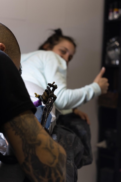 Photo verticale d'une jeune femme caucasienne floue faisant des gestes d'être bien alors qu'elle est tatouée par un homme en studio