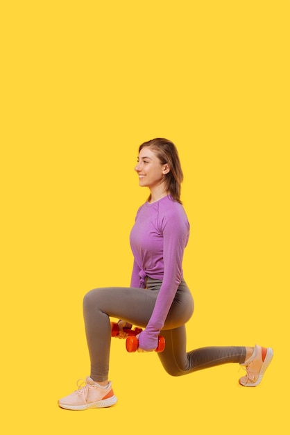 Photo verticale d'une jeune femme effectuant des mouvements brusques avec des haltères dans un studio