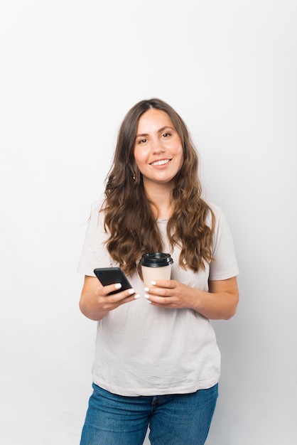 Photo verticale d'une jeune femme tenant son téléphone et une tasse de café à emporter.