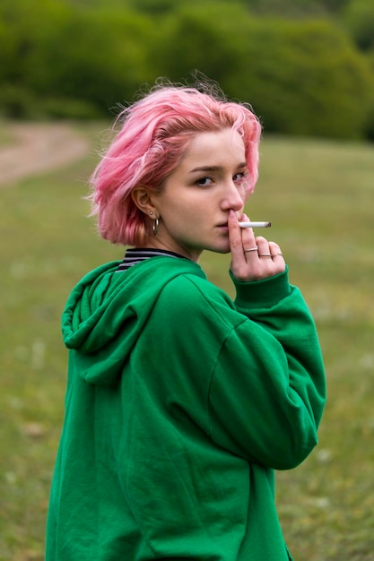 Photo verticale d'une jeune fille aux cheveux roses fumant et regardant la caméra