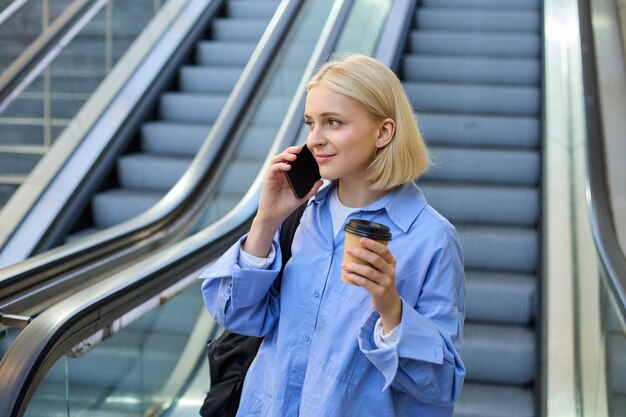 Photo une photo de vie d'une jeune étudiante qui parle au téléphone portable en buvant du café debout.