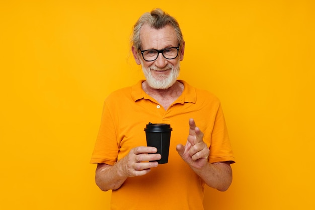 Photo d'un vieil homme à la retraite dans un t-shirt jaune un verre avec une boisson fond isolé