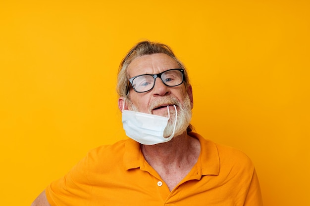 Photo d'un vieil homme à la retraite masque médical dans une chemise jaune fond isolé