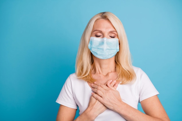 Photo d'une vieille femme calme et paisible mettre ses mains sur la poitrine porter un masque bon look vêtements isolés sur fond de couleur bleu