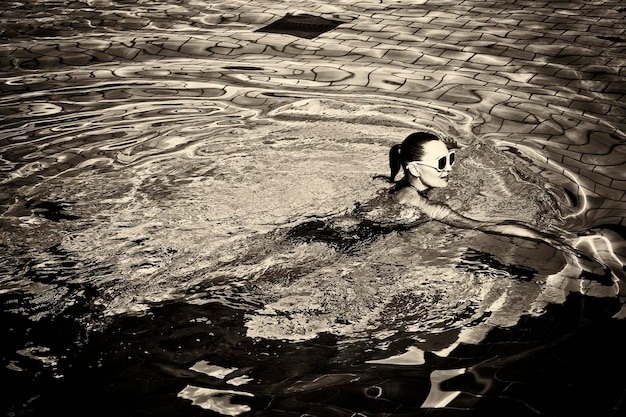 Photo vintage d'une femme en maillot de bain noir et lunettes de soleil blanches nageant dans la piscine