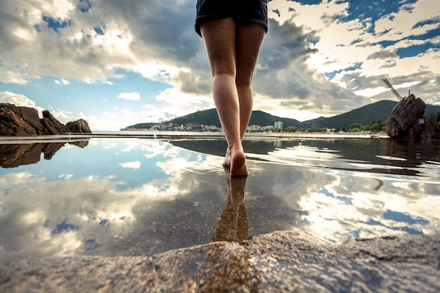 Photo vue arrière de belles jambes féminines minces marchant sur la surface de l'eau avec un ciel réfléchissant