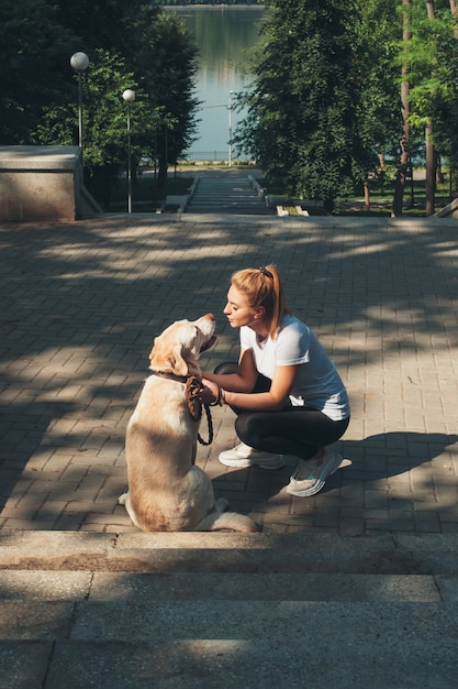 Photo vue arrière d'une femme blonde caucasienne embrassant son golden retriever lors d'une promenade dans le parc