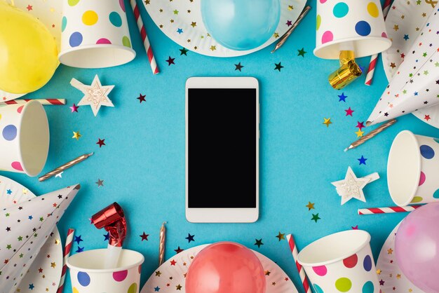 Photo vue de dessus des accessoires de fête de composition de table d'anniversaire et smartphone avec fond au milieu sur fond bleu isolé