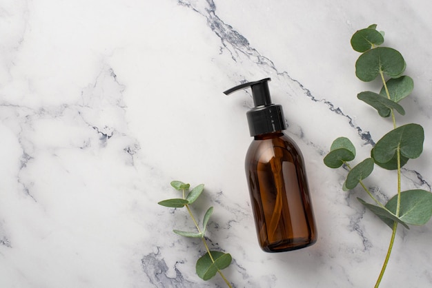 Photo vue de dessus d'une bouteille distributrice en verre avec des cosmétiques naturels et de l'eucalyptus sur fond de marbre blanc avec fond