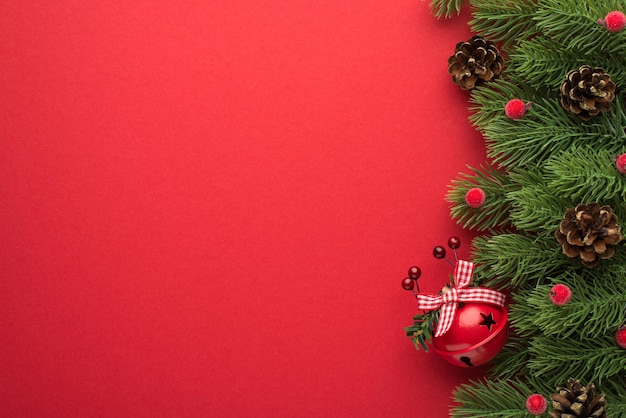 Photo vue de dessus de branches de pin avec cônes de baies rouges et cloche de noël rouge avec arc sur fond rouge isolé avec espace pour copie