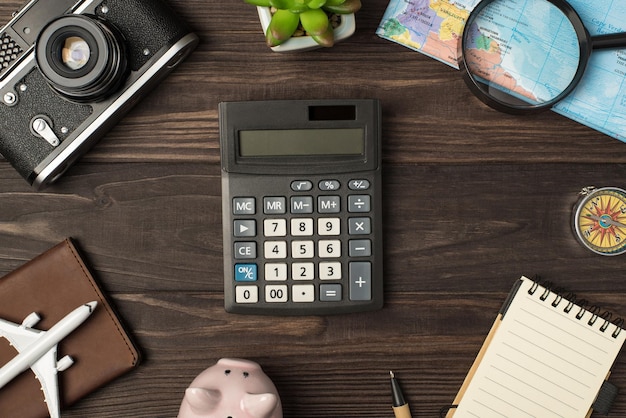 Photo vue de dessus de la calculatrice au centre tirelire avion modèle appareil photo carte loupe boussole passeport couverture stylo plante et cahier sur fond de table en bois isolé