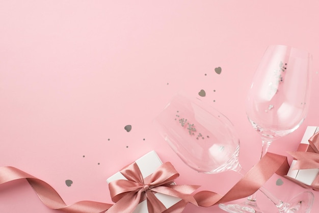 Photo vue de dessus de coffrets cadeaux blancs avec ruban de soie rose arcs deux verres à vin paillettes argentées et confettis en forme de coeur sur fond rose pastel isolé avec fond