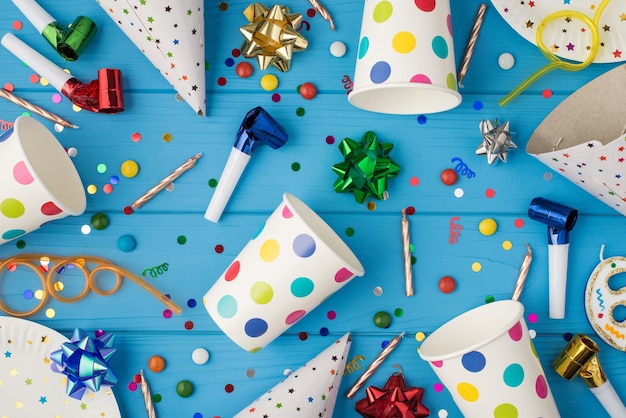 Photo vue de dessus de la composition de la fête d'anniversaire tubes à cocktail en spirale ruban multicolore étoiles bougies rayées tuyaux chapeaux confettis pois tasses en papier et assiettes fond de table en bois bleu isolé