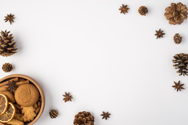 Photo vue de dessus de la composition d'hiver cônes de pin anis et bol en bois avec biscuits bâtons de cannelle et tranches de citron séchées sur fond blanc isolé avec un espace vide au milieu