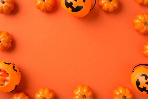 Photo vue de dessus des décorations d'halloween paniers de citrouille avec des bonbons au maïs sur fond orange isolé avec espace pour copie au milieu