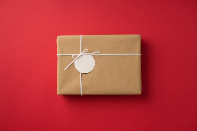 Photo vue de dessus des décorations de la saint-valentin boîte cadeau en papier kraft avec petit arc et étiquette de prix sur fond rouge isolé avec espace vide