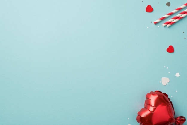 Photo vue de dessus des décorations de la saint-valentin pailles confettis de ballon en forme de coeur et paillettes sur fond bleu pastel isolé avec fond