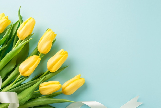 Photo vue de dessus du bouquet de composition de la journée de la femme de tulipes jaunes et ruban blanc sur fond bleu pastel isolé avec fond