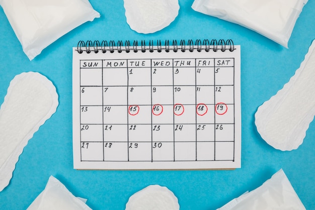 Photo vue de dessus du calendrier des dames de serviettes hygiéniques avec des marques sur fond bleu isolé Le concept des règles des femmes