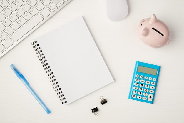 Photo vue de dessus du lieu de travail d'affaires avec clavier souris tirelire liants cahier avec calculatrice bleue copyspace et stylo sur fond blanc isolé