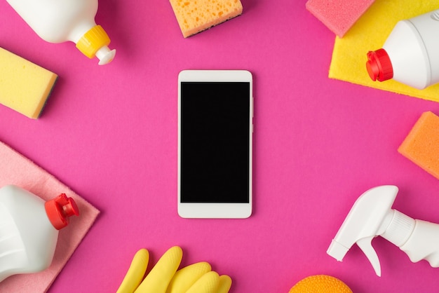 Photo Vue De Dessus Du Smartphone Au Milieu Des Tampons à Récurer Chiffons Gants En Caoutchouc Et Bouteilles De Détergent Blanc Sur Fond Rose Isolé Avec Espace Pour Copie