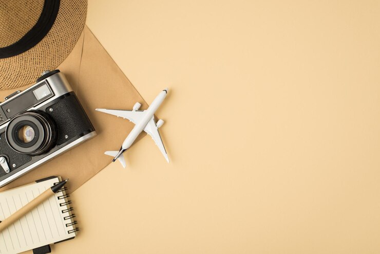 Photo vue de dessus du stylo couvre-chef sur l'appareil photo du cahier et le modèle d'avion sur l'enveloppe en papier kraft sur fond beige isolé avec espace pour copie