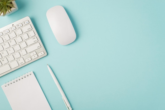 Photo vue de dessus du stylo de rappel de la souris du clavier blanc et du pot de fleurs sur fond bleu pastel isolé avec espace pour copie