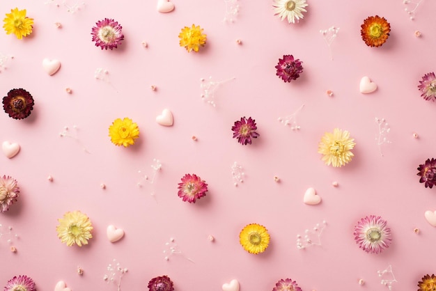 Photo vue de dessus des nombreuses fleurs colorées différentes avec des branches de gypsophile et des confettis de volume rose en forme de coeurs éparpillés sur le fond rose pastel