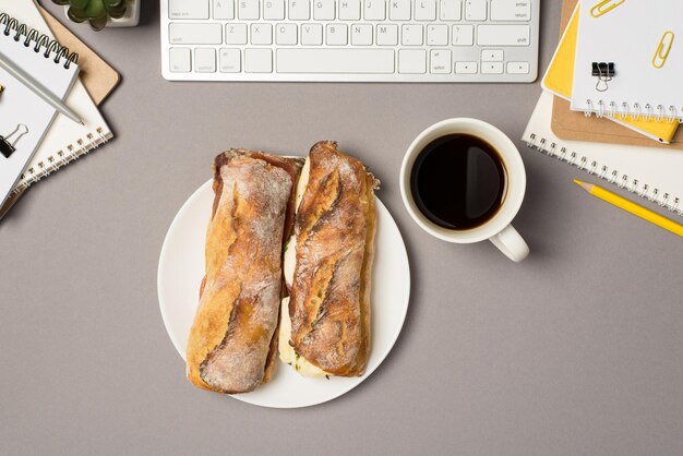 Photo vue de dessus des planificateurs de clavier d'espace de travail pinces à reliure crayon jaune stylo pot de fleurs tasse de café et assiette avec deux sandwichs sur fond gris isolé