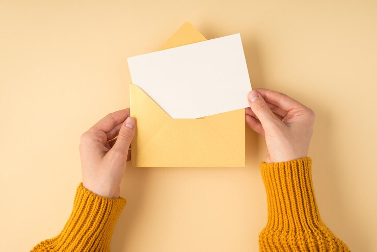 Photo vue de dessus à la première personne de mains féminines en pull jaune tenant une enveloppe jaune pastel ouverte avec carte blanche sur fond orange clair isolé avec espace pour copie