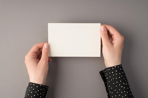 Photo vue de dessus à la première personne des mains d'une femme tenant une carte en papier blanc sur fond gris isolé avec espace pour copie