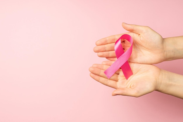 Photo vue de dessus à la première personne des mains de la jeune fille tenant un ruban de satin rose dans les paumes symbole de la sensibilisation au cancer du sein sur fond rose pastel isolé avec espace vide