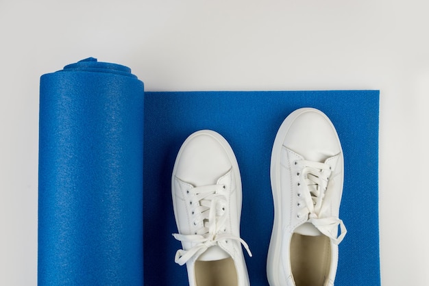 Photo photo vue de dessus d'un tapis de fitness bleu et de baskets blanches sur fond blancle concept de fitness yoga sports