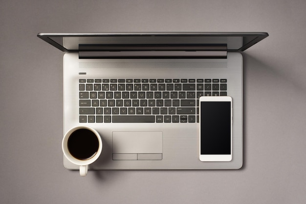 Photo vue de dessus d'une tasse de boisson et d'un smartphone sur un ordinateur portable gris ouvert sur fond gris isolé avec espace vide