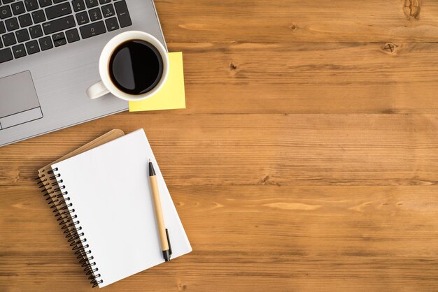 Photo vue de dessus d'une tasse de café papier autocollant jaune sur ordinateur portable et stylo sur deux cahiers en spirale sur fond de table en bois isolé avec espace vide