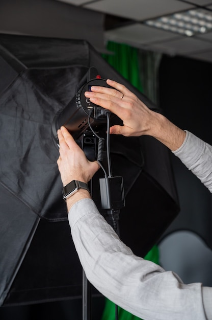 Le photographe ajuste l'intensité lumineuse de la boîte à lumière en studio. L'homme réglage de l'équipement de photographie se prépare pour une séance photo.