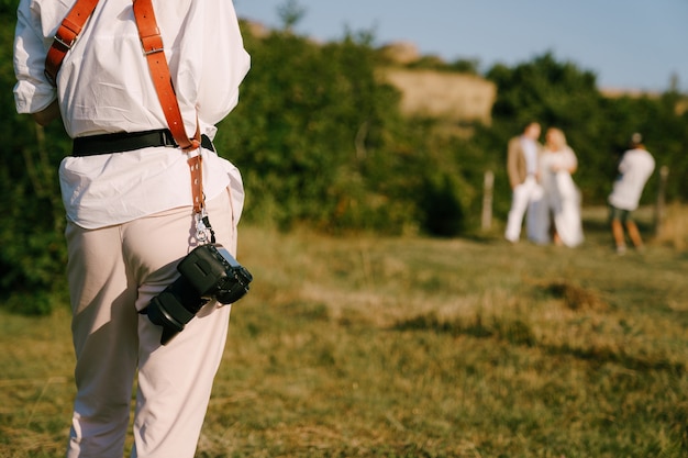 Le photographe avec un appareil photo à la ceinture prend une vue arrière de deux jeunes mariés