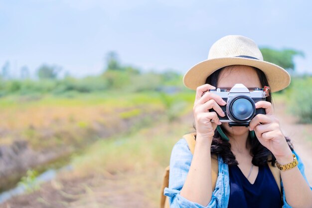 Photographe asiatique couvrant son visage avec l'appareil photo Portrait d'une jolie fille joyeuse avec des cheveux noirs étonnants plaçant une caméra extérieure une femme se reposant dans le jardin