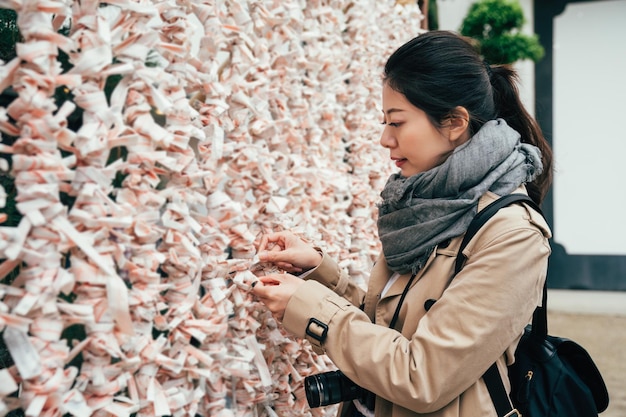 un photographe asiatique découvre la culture traditionnelle japonaise à tenmangu osaka au japon. la jeune femme attache le feuillet de fortune au mur pour laisser le mauvais sort s'éloigner d'elle. routard fille avec appareil photo.