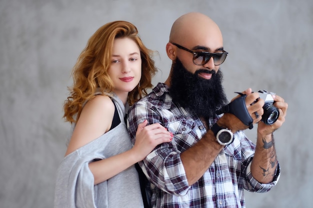 Photographe barbu amateur et une femme rousse posant sur fond gris clair.